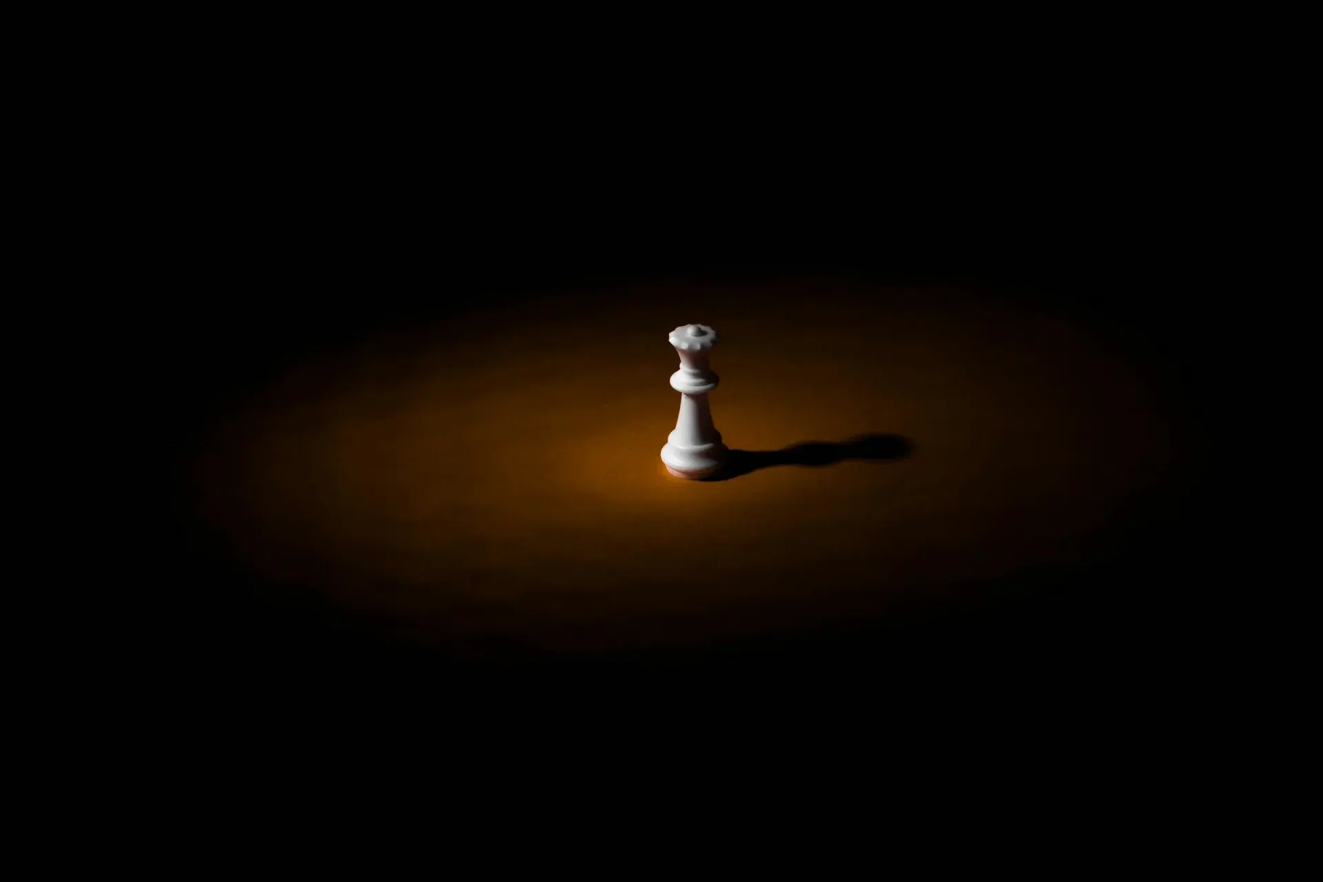 A single white chess piece under a warm orange spotlight on a black background